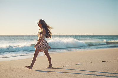 Buy stock photo Shot of a young woman taking a stroll on the beach