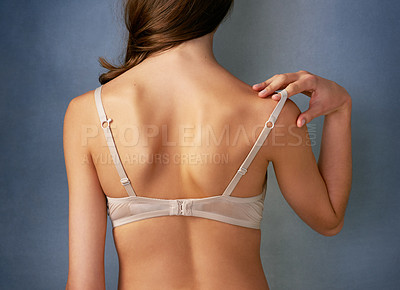 Buy stock photo Rearview shot of an unidentifiable young woman taking off her bra in studio