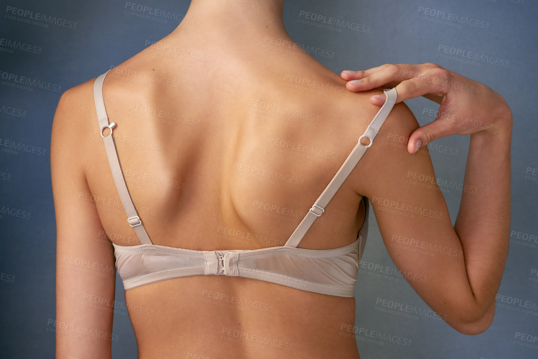 Buy stock photo Rearview shot of an unidentifiable young woman taking off her bra in studio