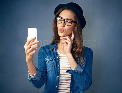 Buy stock photo Shot of a quirky young woman taking a selfie with her smartphone in studio