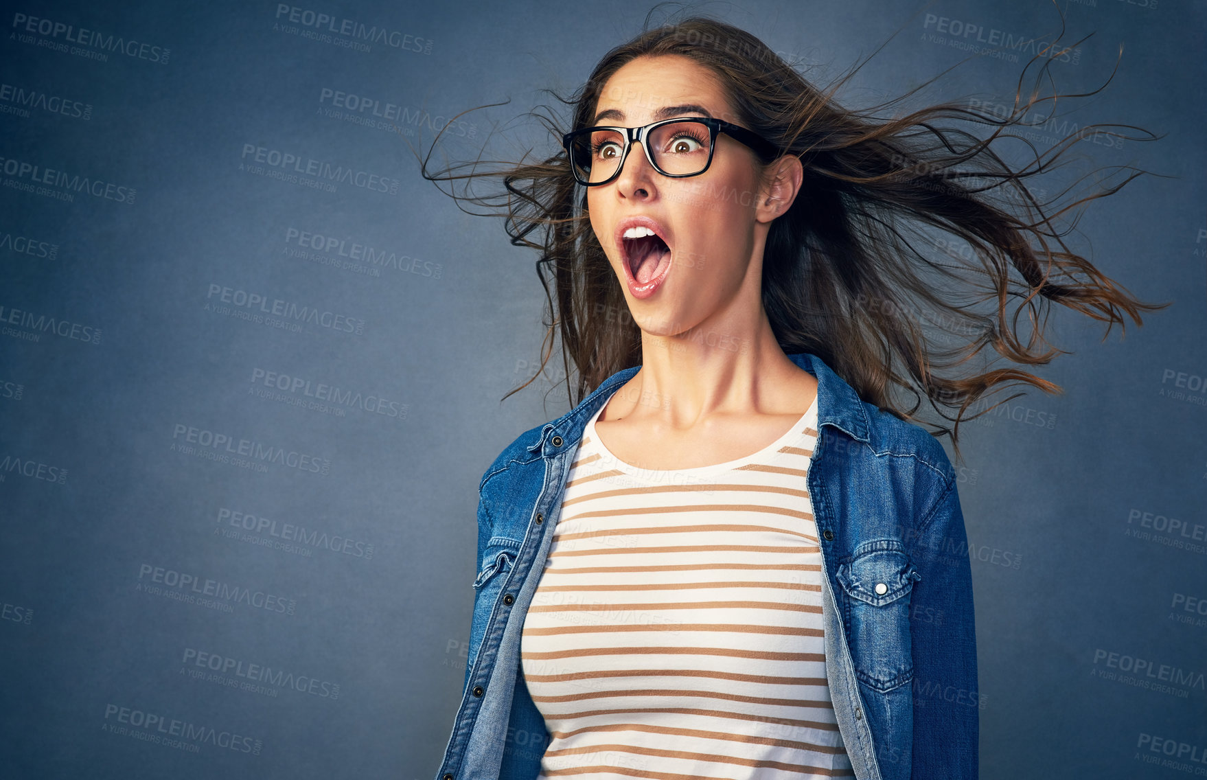 Buy stock photo Shot of a happy young woman with air being blown in her face in studio