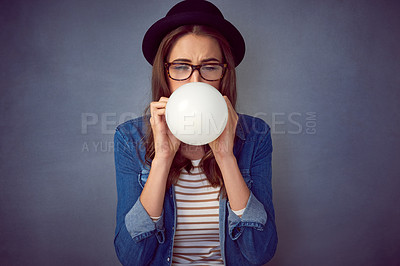 Buy stock photo Shot of a fun-loving young woman blowing up a balloon in studio