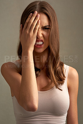 Buy stock photo Studio portrait of an expressive young woman covering half of her face with her hand