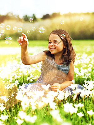 Buy stock photo Shot of an adorable little girl playing with bubbles while sitting in a field of wildflowers outside