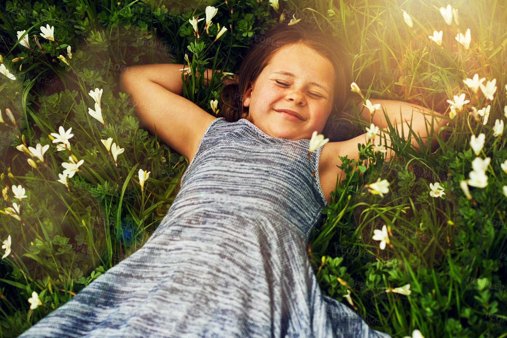 Buy stock photo Shot of a cute little girl lying in a field of wildflowers outside