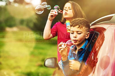 Buy stock photo Shot of two happy children blowing bubbles while leaning out of a car window together