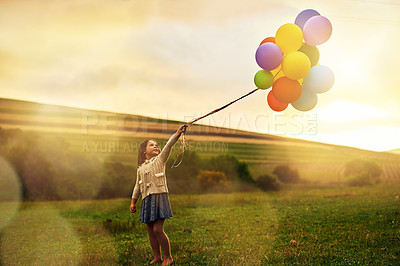 Buy stock photo Shot of a playful little girl walking through a field while holding a bunch of balloons
