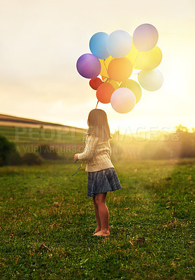 Buy stock photo Shot of a playful little girl walking through a field while holding a bunch of balloons
