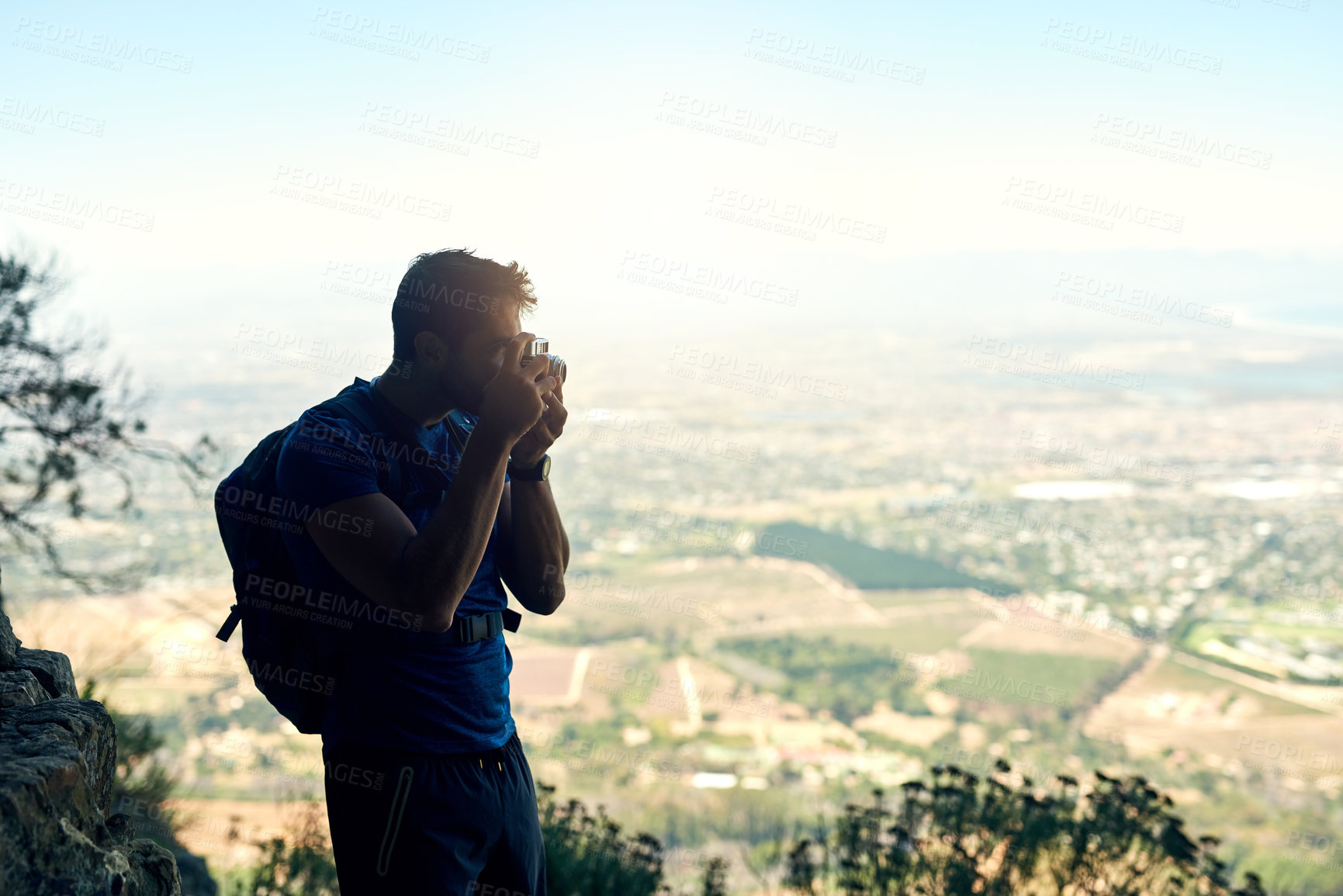 Buy stock photo Rear view shot of a young man taking a photo of the scenic view from the top of a mountain