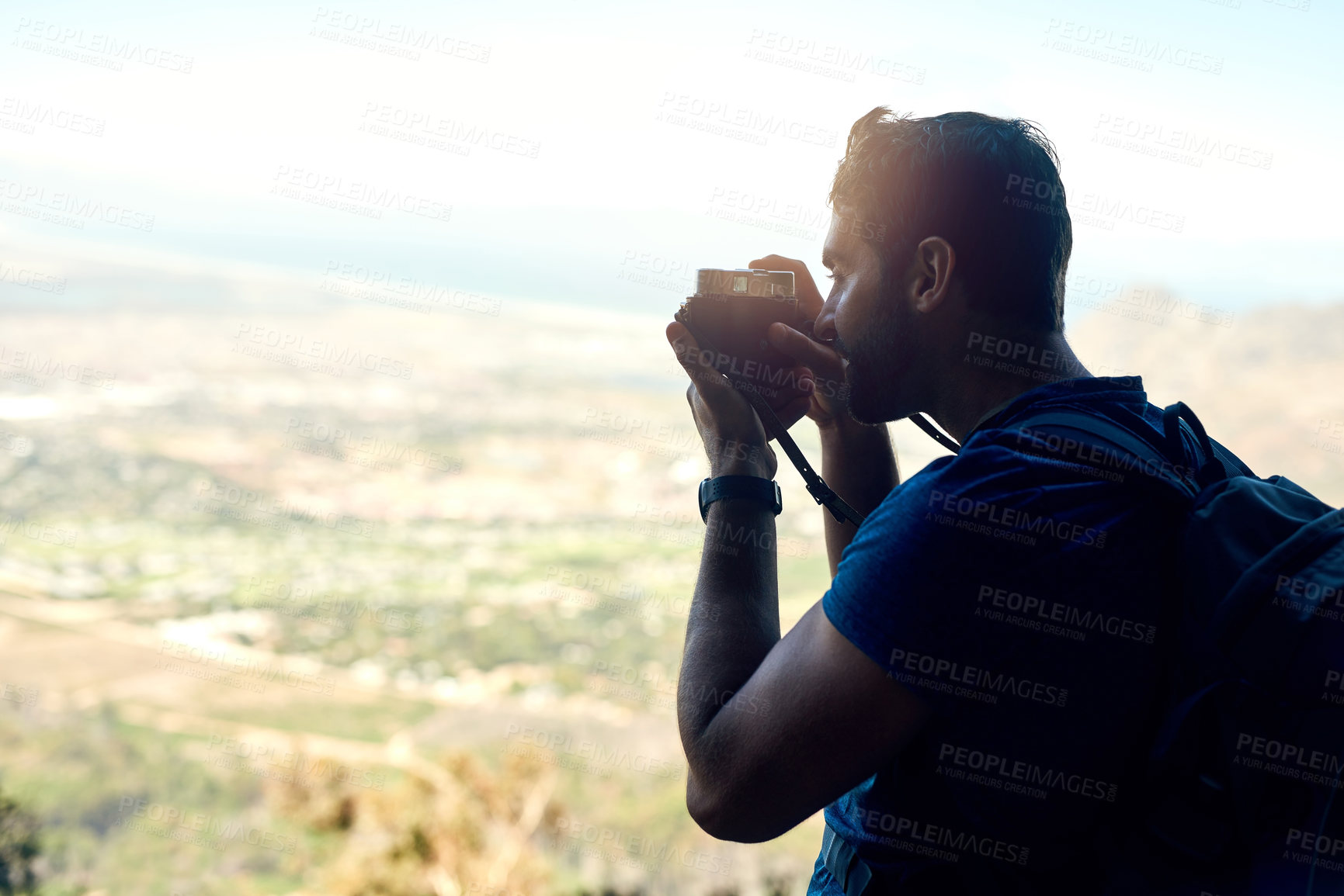 Buy stock photo Rear view shot of a young man taking a photo of the scenic view from the top of a mountain