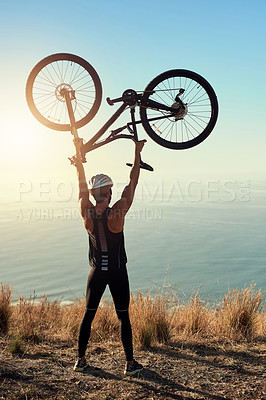 Buy stock photo Rearview shot of a male cyclist lifting his mountain bike into the air
