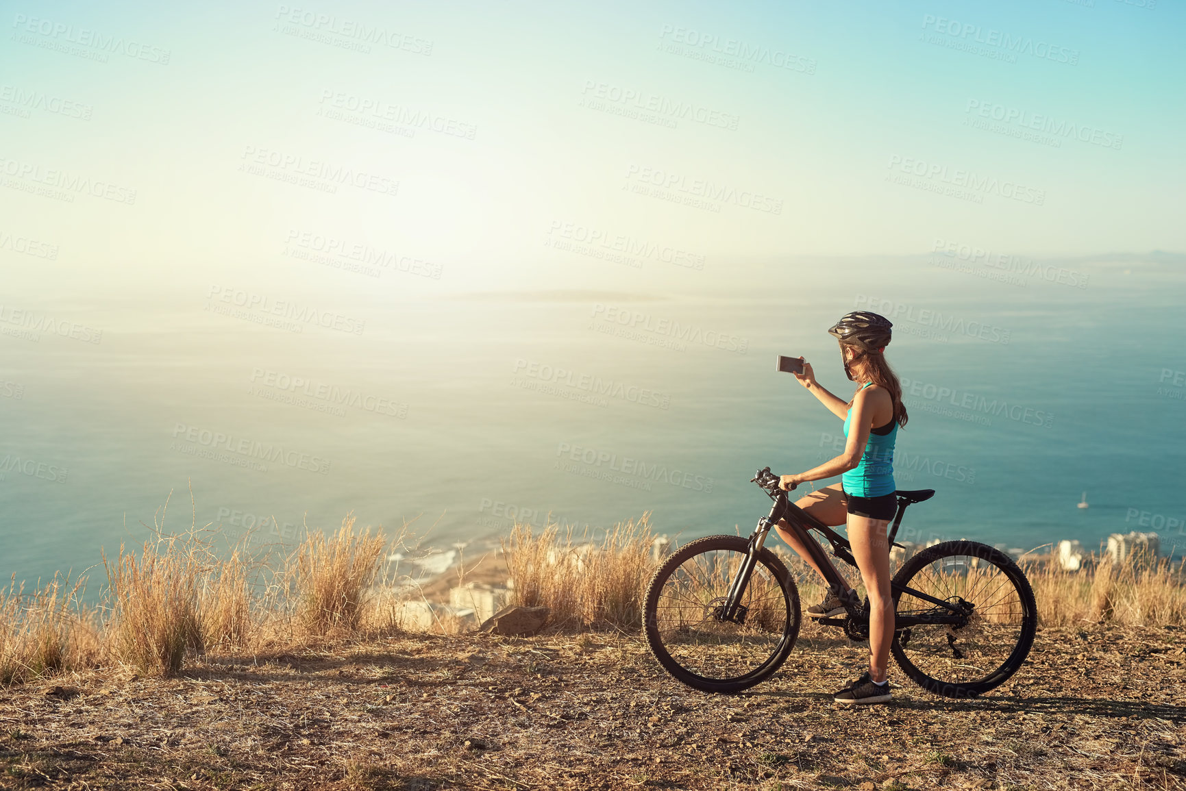 Buy stock photo Shot of a young woman taking a picture of the beautiful scenery while out mountain biking