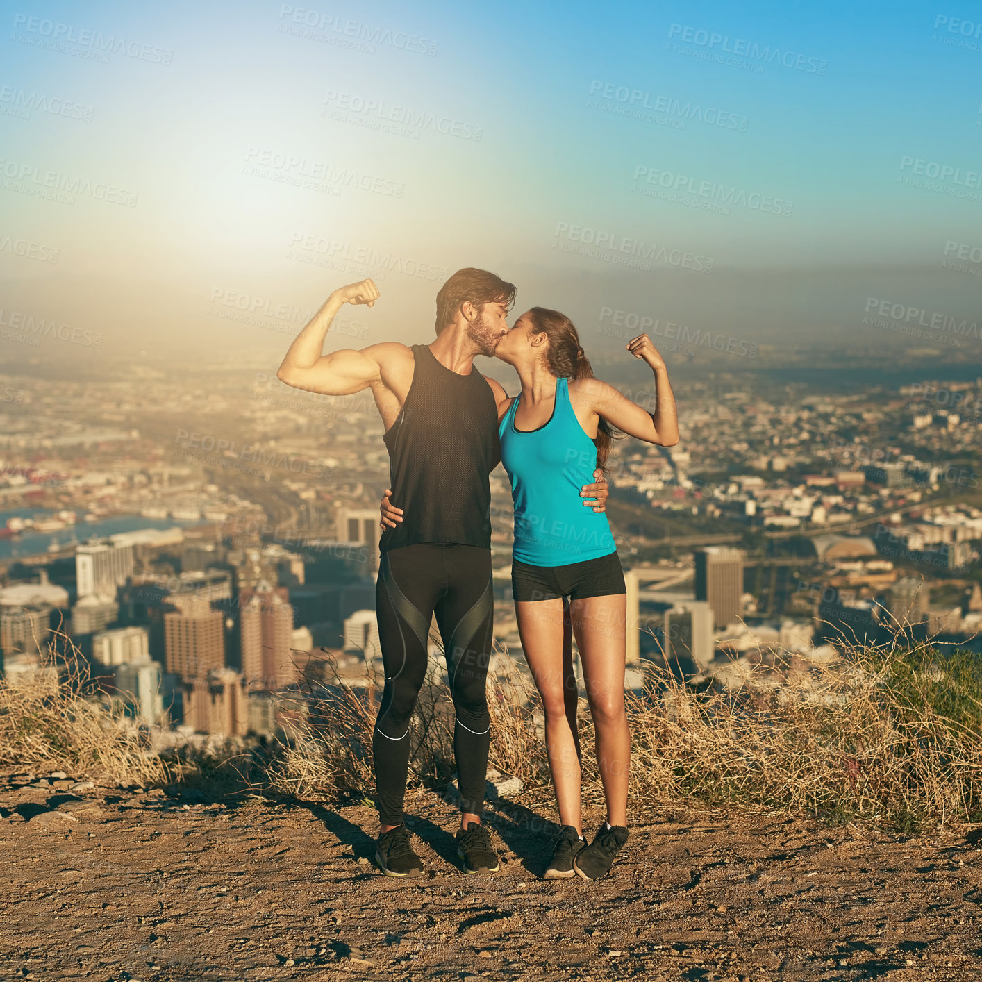 Buy stock photo Man, woman and kiss or flex in outdoor on mountain with city background, workout and strength together for motivation. Couple, training and bonding with fitness in nature, active and love for cardio.