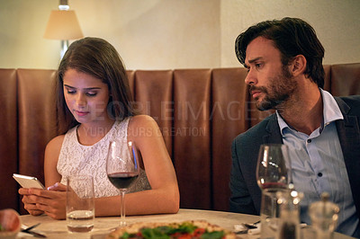 Buy stock photo Phone, chatting and couple on a date at a restaurant for valentines day, romance or anniversary. Communication, upset and annoyed man watching his girlfriend sitting on her cellphone at dinner.