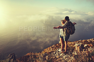 Buy stock photo Shot of an adventurous young couple admiring the view from a mountain peak while out on a hike