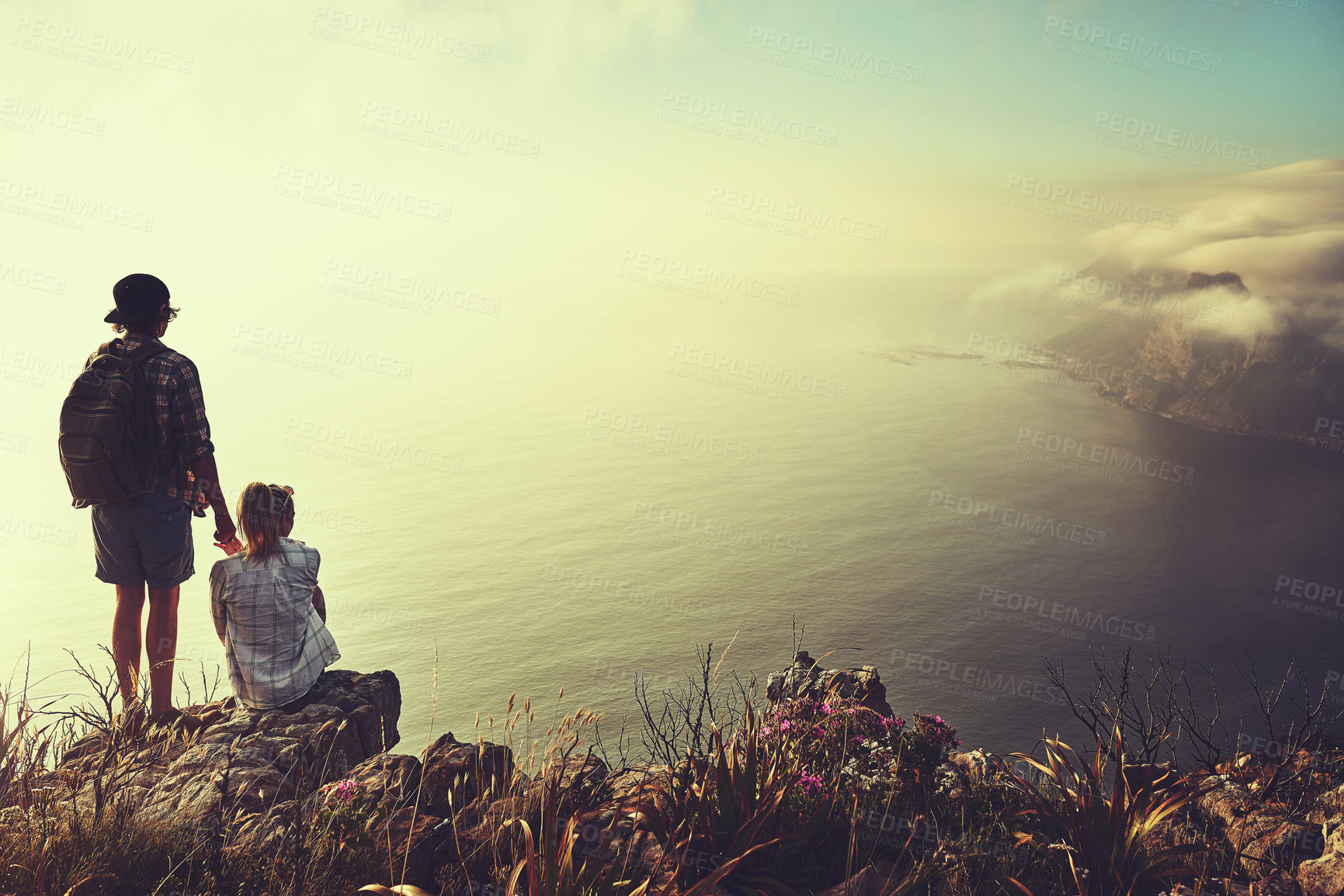 Buy stock photo Rearview shot of an unidentifiable young couple admiring the view from a mountain peak together