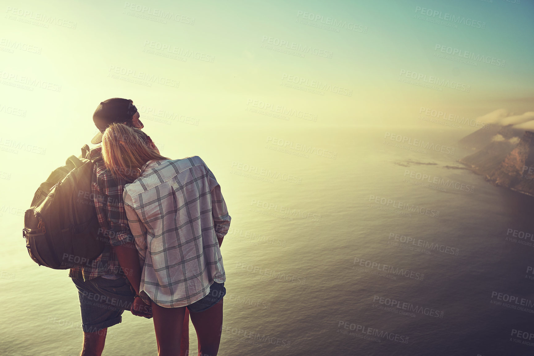 Buy stock photo Rearview shot of an unidentifiable young couple admiring the view from a mountain peak together