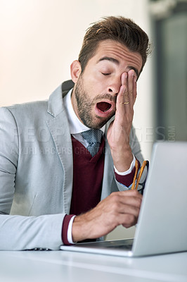 Buy stock photo Shot of a tired businessman yawning while using a laptop at his office desk