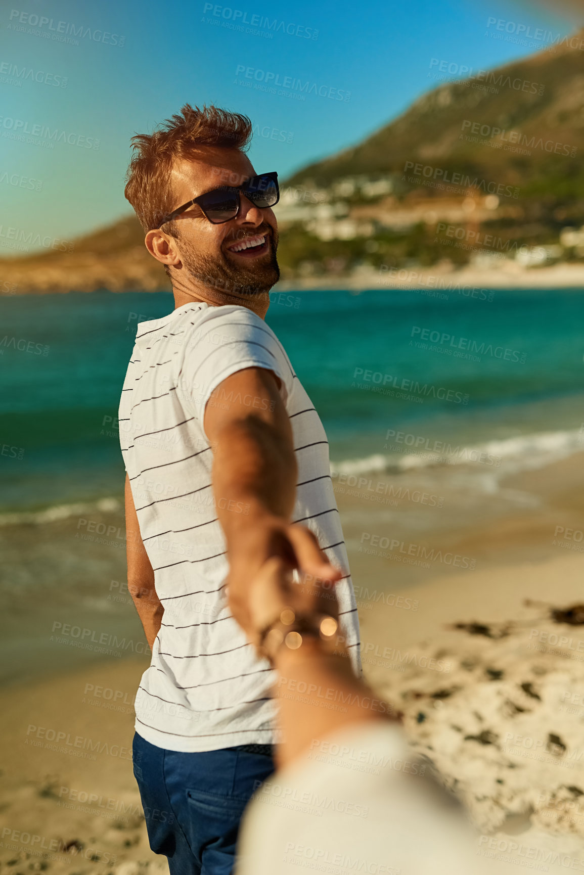 Buy stock photo Shot of a young man holding his girlfriend’s hand and leading the way at the beach