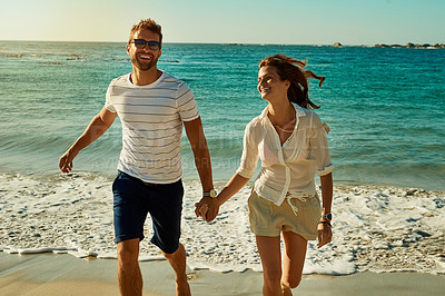 Buy stock photo Shot of a happy young couple running along the beach