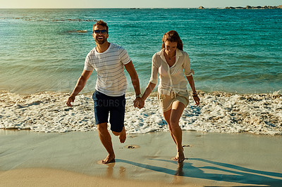 Buy stock photo Shot of a happy young couple running along the beach