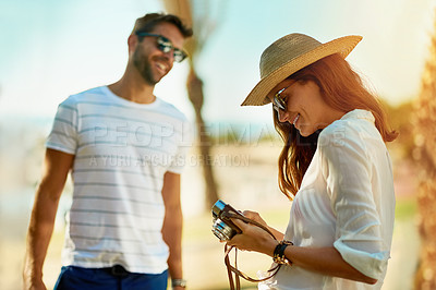 Buy stock photo Shot of an young woman taking pictures of her boyfriend with a camera on a summer’s day outdoors