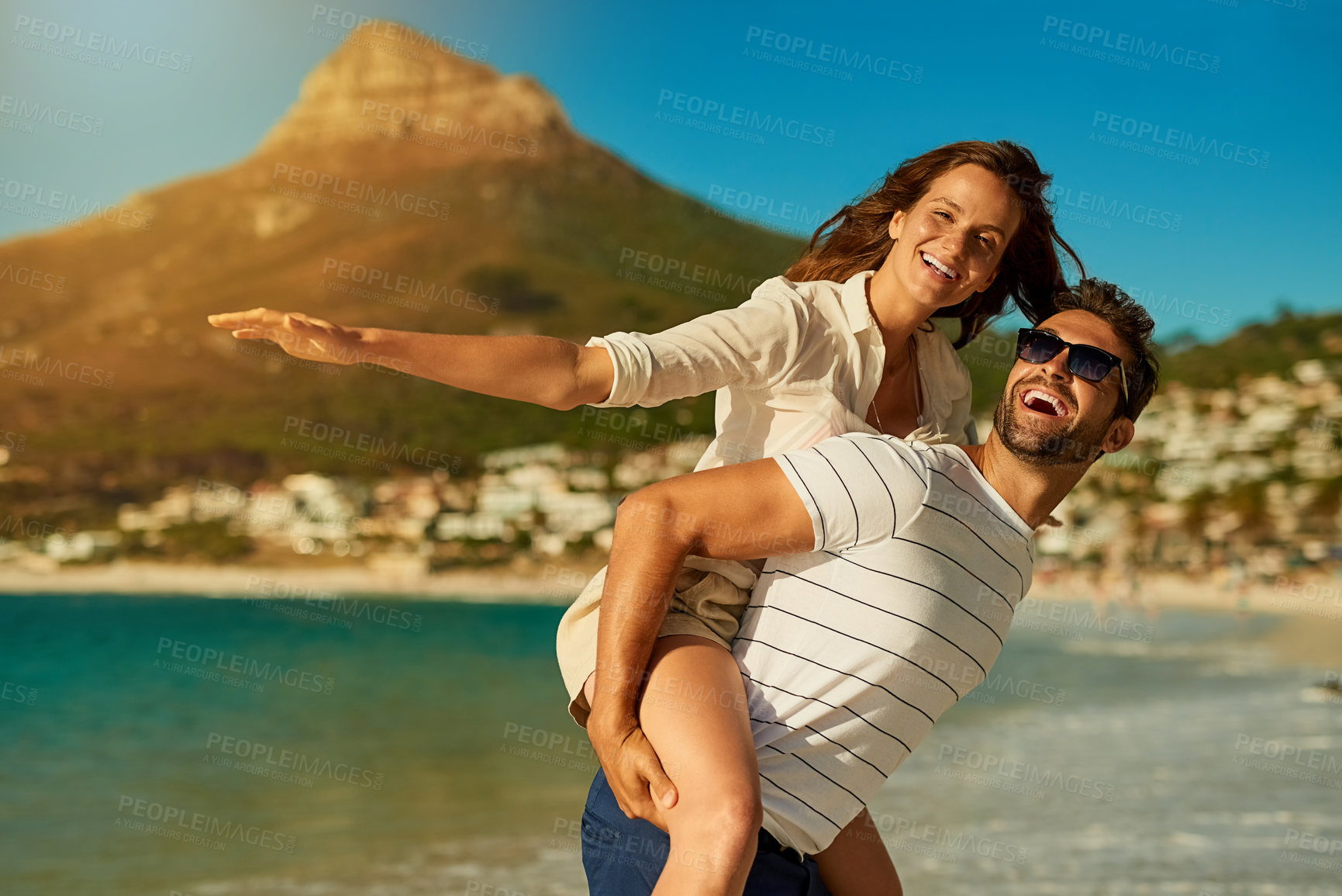 Buy stock photo Portrait, couple and piggyback by ocean for love, commitment and bonding on summer vacation for honeymoon. Man, woman and freedom on beach for romantic holiday, airplane and weekend with energy.