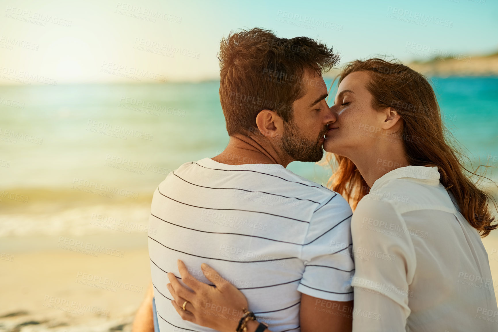 Buy stock photo Kiss, couple and relax on beach for love, commitment and bonding on summer vacation for honeymoon. Man, woman and back view together by ocean for romantic holiday, affection and weekend with embrace.