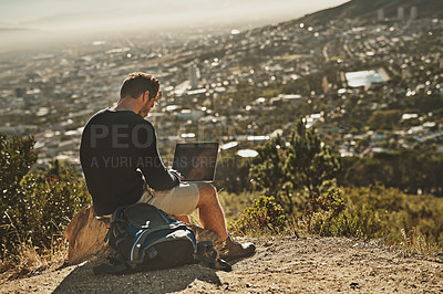 Buy stock photo Shot of a young man using his laptop while sitting on a mountain top