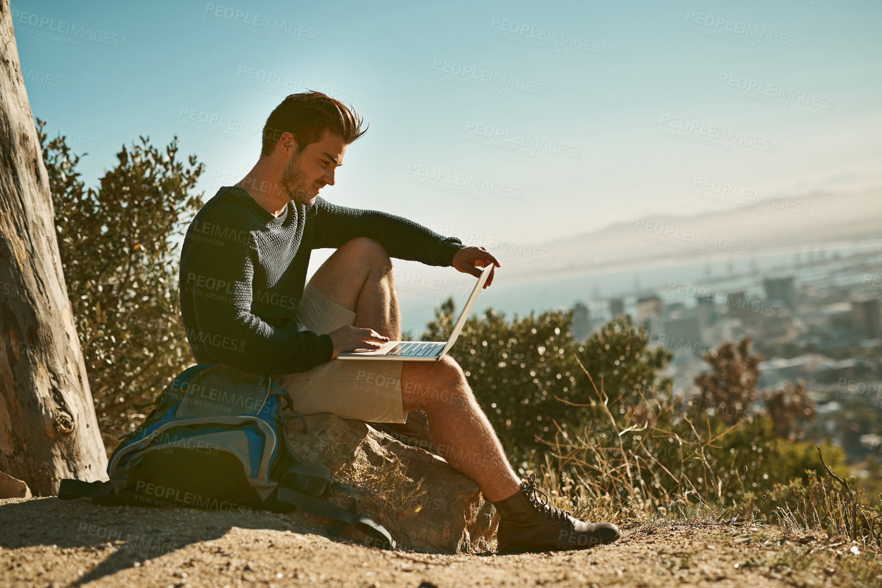 Buy stock photo Shot of a young man using his laptop while sitting on a mountain top