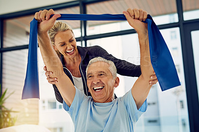 Buy stock photo Shot of a physiotherapist helping a senior patient stretch with a stretch band in her office