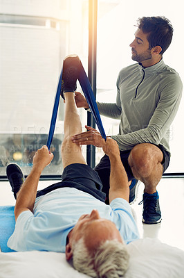 Buy stock photo Shot of a physiotherapist helping a senior patient stretch his legs with a stretch band in his office