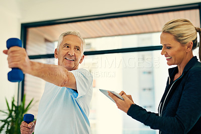 Buy stock photo Shot of a happy physiotherapist tracking her senior patient's progress on a tablet while he lifts weights