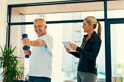 Buy stock photo Shot of a happy physiotherapist tracking her senior patient's progress on a tablet while he lifts weights