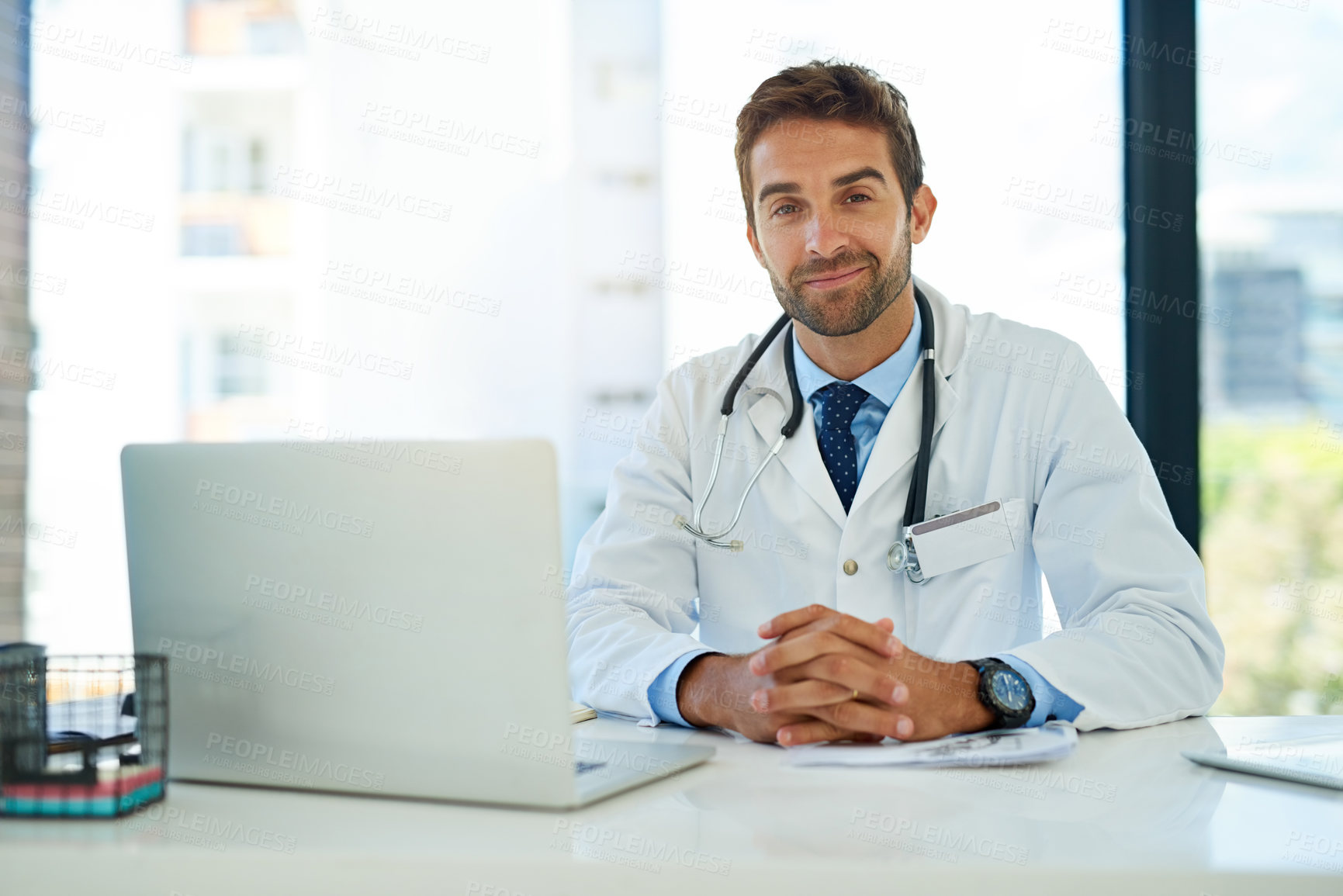 Buy stock photo Portrait of a happy doctor using his laptop while sitting at his desk