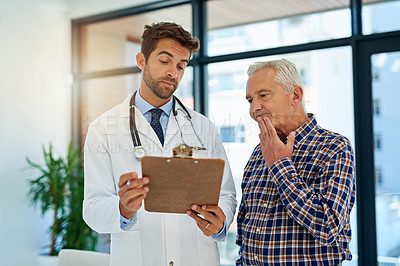 Buy stock photo Shot of a doctor and his mature patient considering test results on a clipboard in the hospital