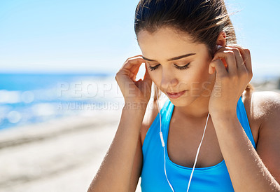 Buy stock photo Cropped shot of a young woman listening to music while out for a run by the sea