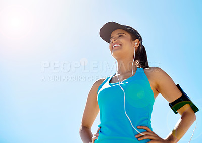Buy stock photo Shot of a young woman listening to music while out for a run against a clear blue sky