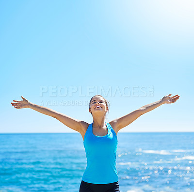 Buy stock photo Shot of a sporty young woman standing with her arms outstretched on the beach