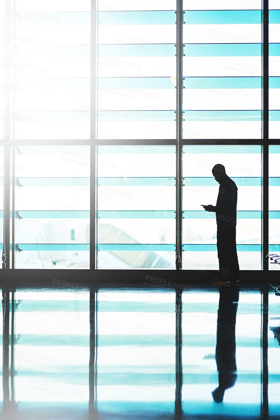 Buy stock photo Shot of an unidentifiable traveler using his smartphone in an empty airport lounge