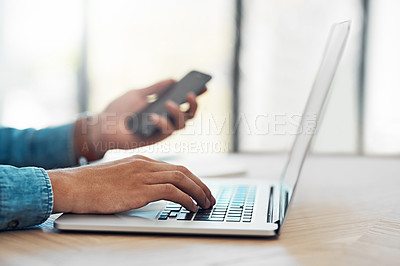 Buy stock photo Shot of an unidentifiable young businessman using his smartphone and laptop at a table in the office