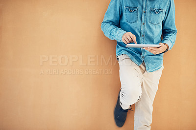 Buy stock photo Shot of an unidentifiable young entrepreneur using his tablet while leaning against a wall in the office