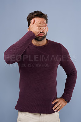 Buy stock photo Studio shot of a young man covering his eyes in regret against a gray background