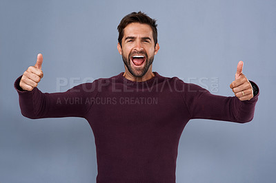 Buy stock photo Studio shot of an enthusiastic young man giving two thumbs up against a gray background
