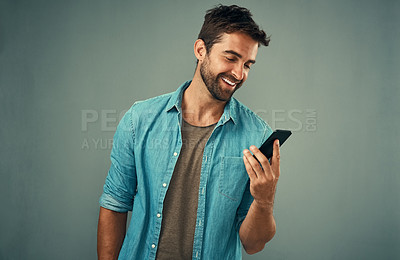 Buy stock photo Studio shot of a handsome young man using a cellphone against a grey background