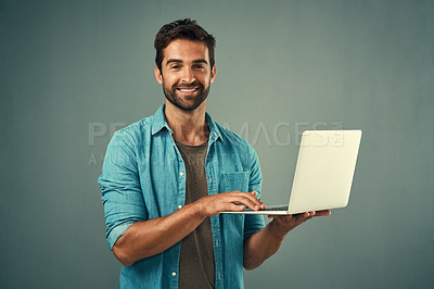 Buy stock photo Studio portrait of a handsome young man using a laptop against a grey background