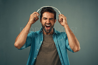 Buy stock photo Studio shot of a handsome young man screaming while holding headphones against a grey background