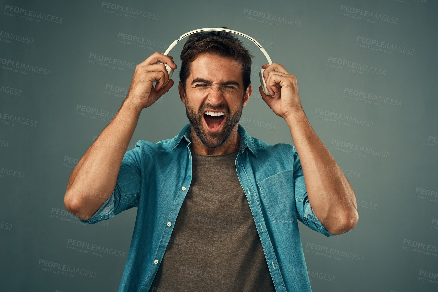 Buy stock photo Studio shot of a handsome young man screaming while holding headphones against a grey background