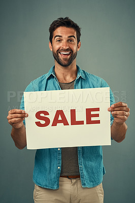 Buy stock photo Studio portrait of a handsome young man holding a sale sign against a grey background