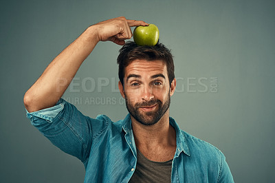 Buy stock photo Studio portrait of a handsome young man posing with an apple on his head against a grey background